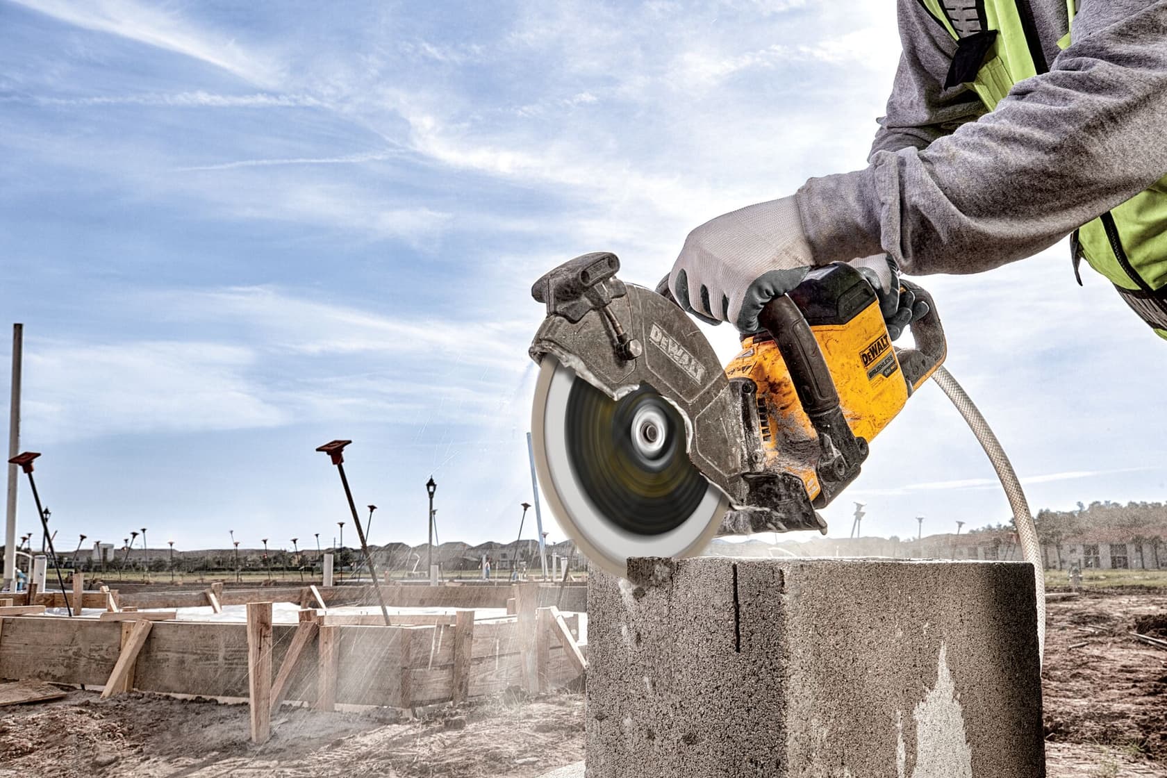 A DEWALT power tool is being used to cut through a concrete block outdoors at a construction site. The person operating the