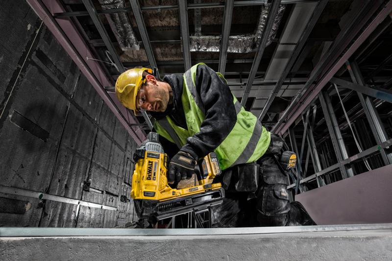 A construction worker wearing a yellow hard hat and green safety vest uses a DEWALT DCN890P2 cordless tool to fasten