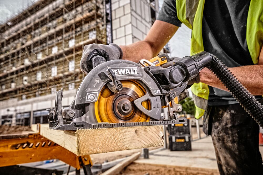 A DEWALT cordless circular saw (model DCS577T2) is being used by a construction worker wearing a safety vest and gloves to