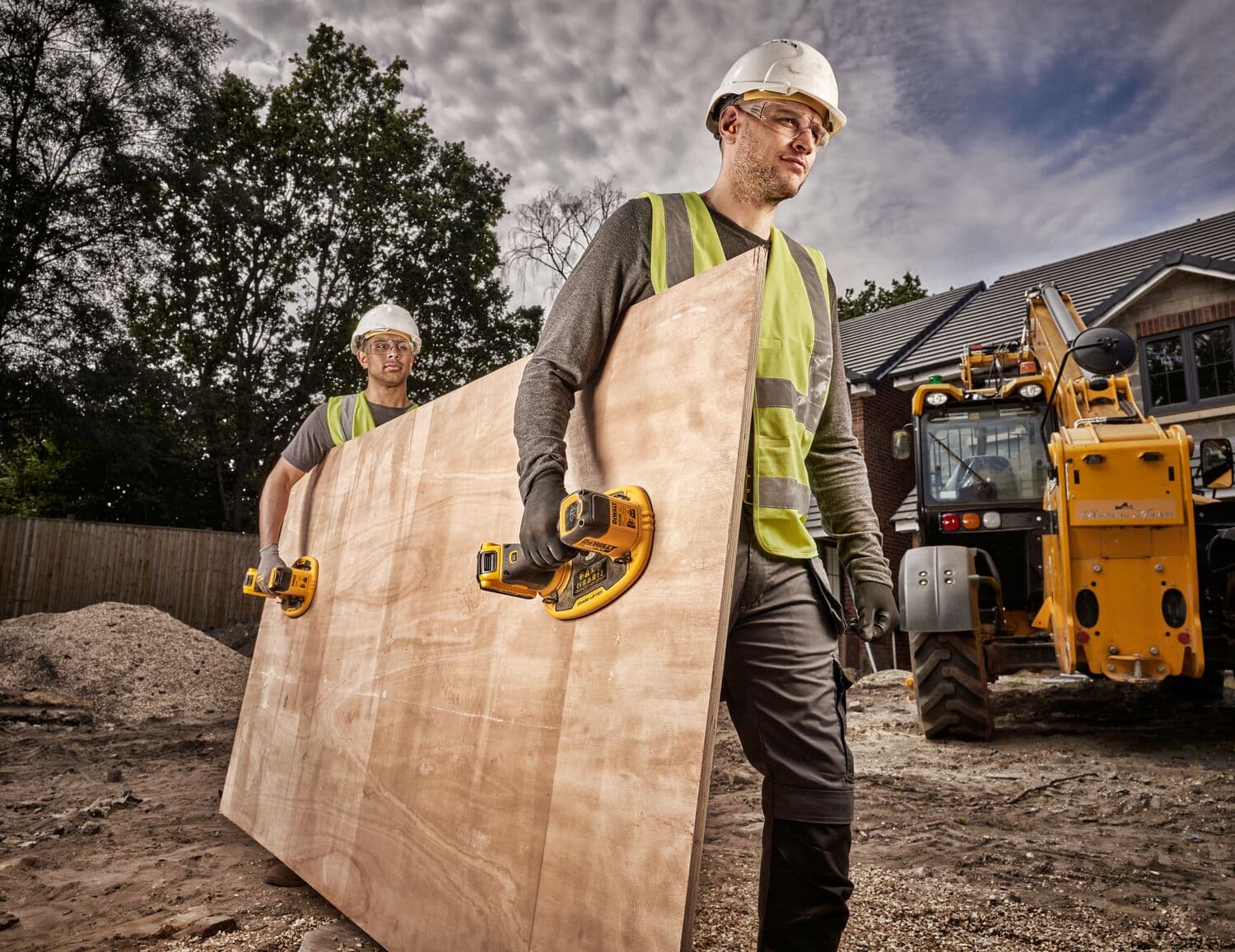 Two construction workers wearing safety helmets and reflective vests use DEWALT DCE590 cordless suction cup tools to carry a