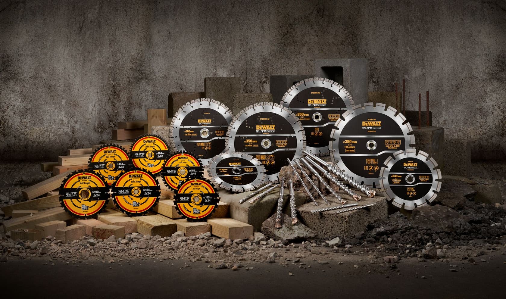 A variety of DEWALT circular saw blades and drill bits are displayed on concrete blocks and wooden planks in front of a rough industrial wall.