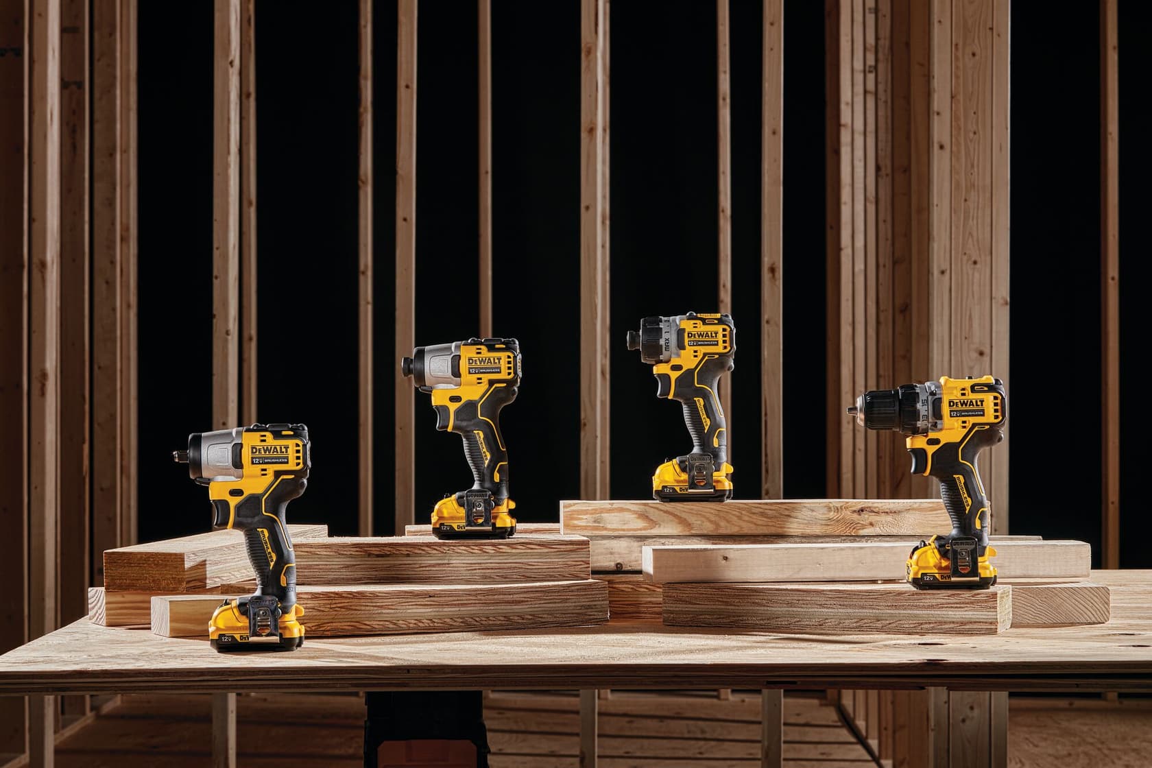 Four DEWALT cordless power drills are displayed on wooden planks in a construction setting with wooden framing in the background.