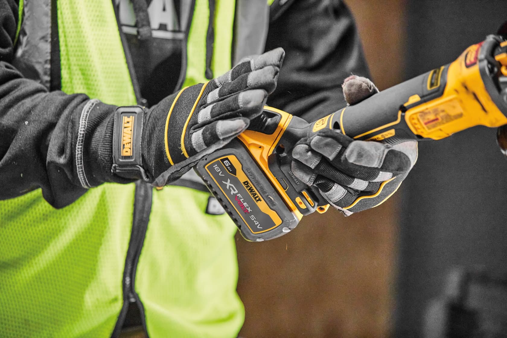 Close-up of a person wearing gloves and a high-visibility vest operating a DEWALT cordless power tool, with an XR FLEXVOLT battery attached.