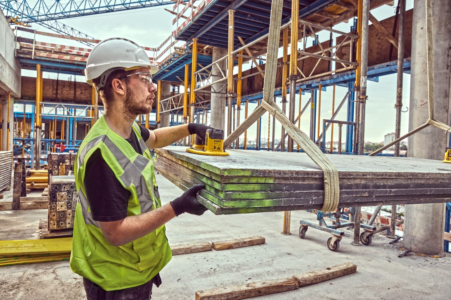A construction worker wearing a safety helmet and reflective vest uses a DEWALT device to assist in lifting concrete panels