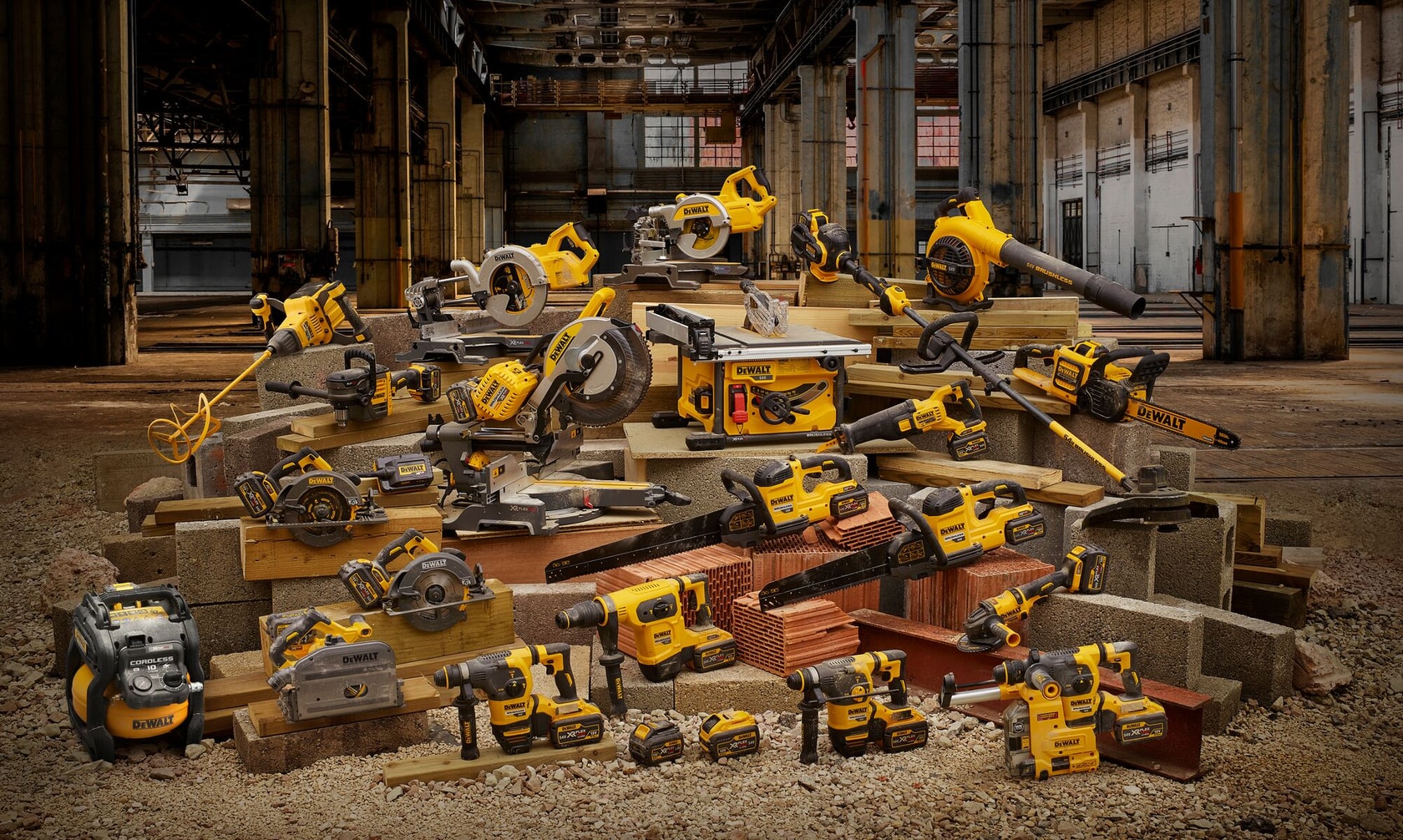 A variety of DEWALT power tools and equipment, including saws, drills, blowers, grinders, and batteries, are arranged on construction materials like bricks and concrete blocks in an industrial warehouse setting.