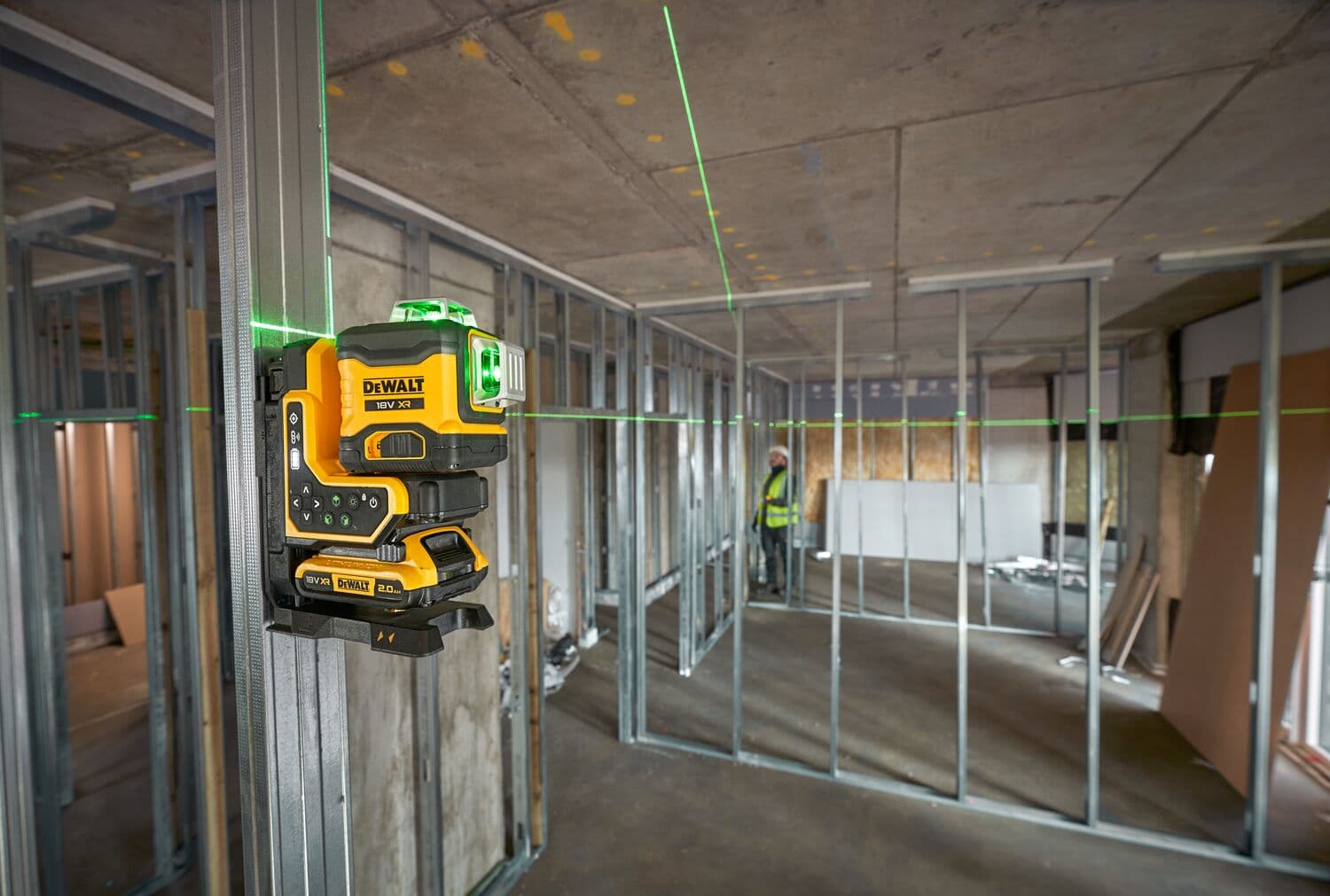 A DEWALT green line laser tool mounted on a metal frame inside a building under construction. The laser projects green lines