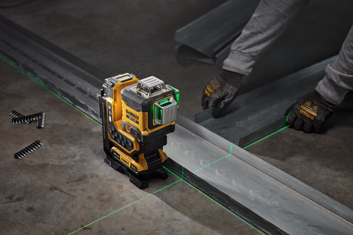 A DEWALT laser level tool with green laser lines is shown on a concrete floor, being used to align metal beams. A person