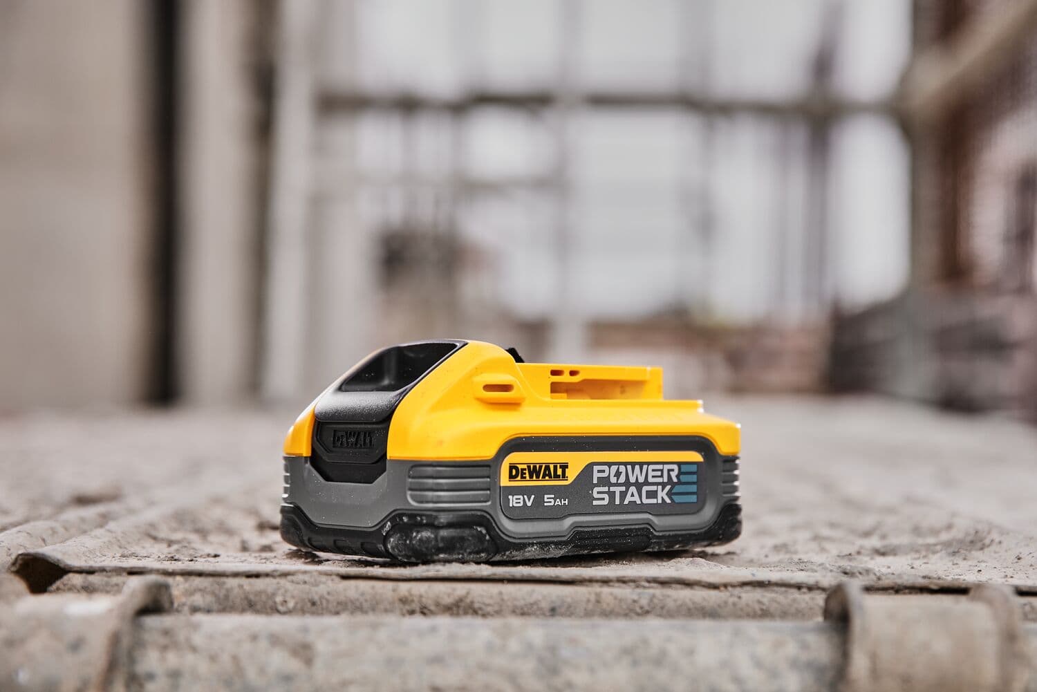 DEWALT POWERSTACK 18V 5Ah battery module placed on a rough concrete surface, photographed in a construction site setting.